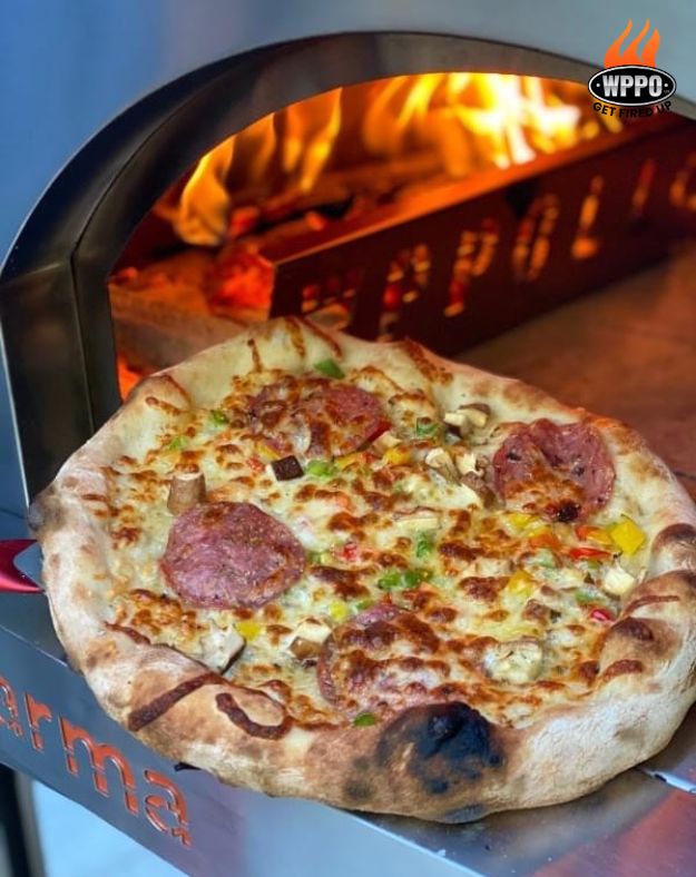 Pizza at the opening of a WPPO Karma oven with a wood fire and metal fire separator inside.