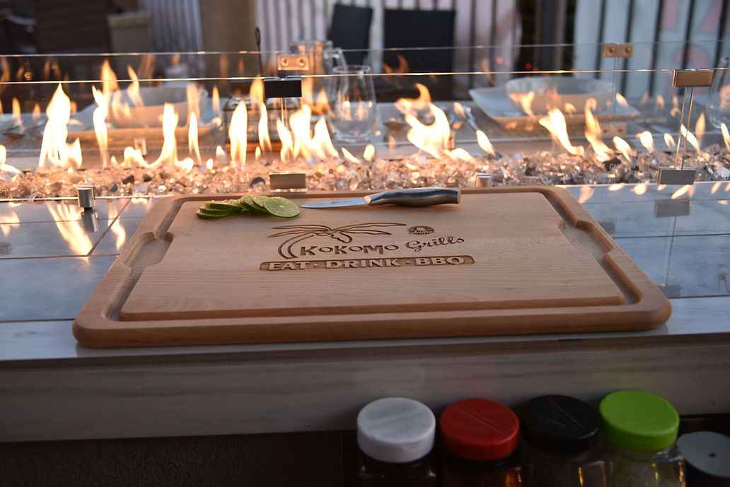 Kokomo cutting board and knife beside the lit countertop fire feature with glass panels.