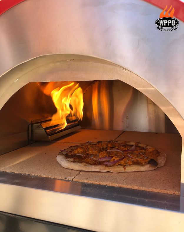 Pizza on the fire brick cooking floor with gas burner flames at the back of the oven.