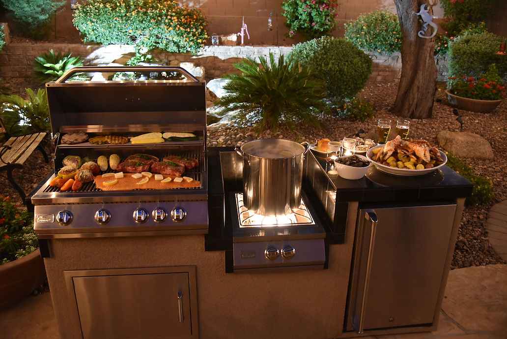 Front view of the Kokomo island at dusk with food on the grill, pot on the wok burner and refrigerator.