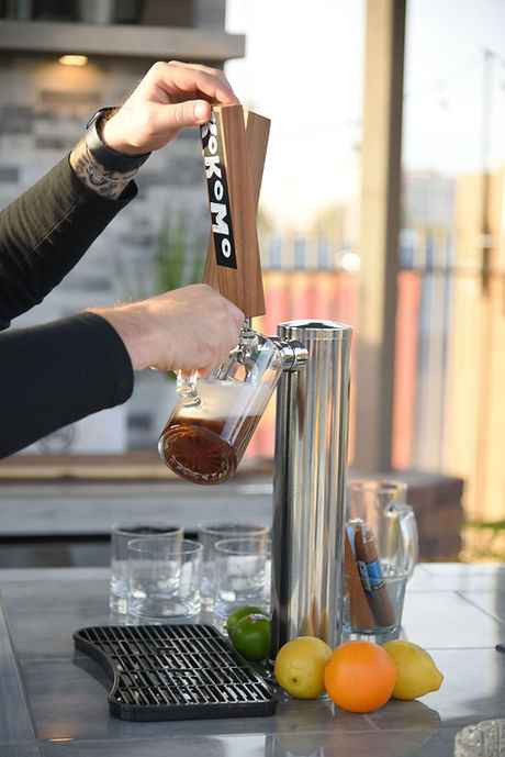 Person pouring a drink from a stainless steel countertop tap with a Kokomo handle.