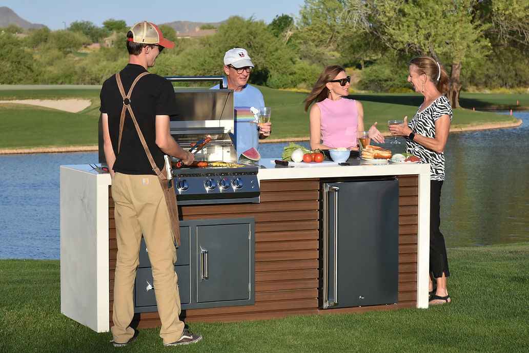 Four people gathering around the Kokomo outdoor kitchen island while grilling beside a pond.