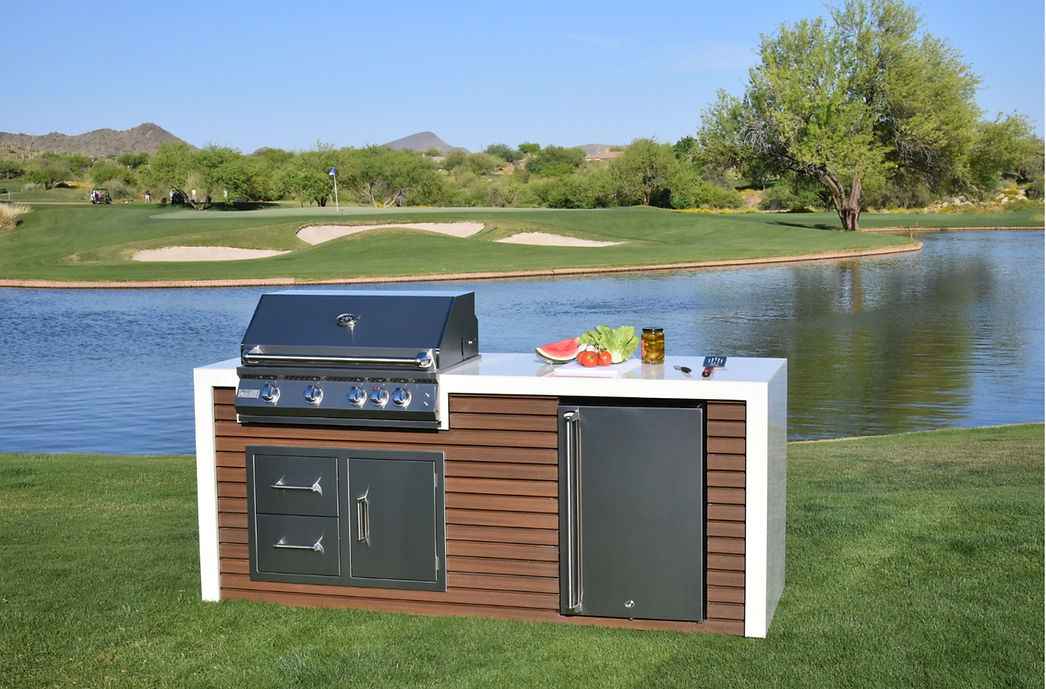 Kokomo outdoor kitchen island with closed grill hood, white waterfall countertop and refrigerator.