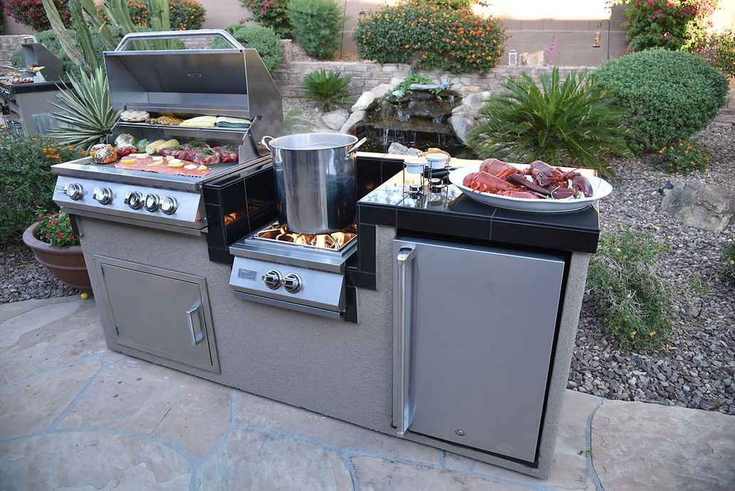Kokomo outdoor kitchen island with open grill, pot on the wok burner and refrigerator on a garden patio