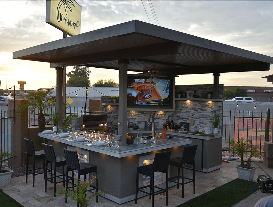 Kokomo Bermuda covered outdoor kitchen with mounted TV, lit countertop fire feature and bar stools.