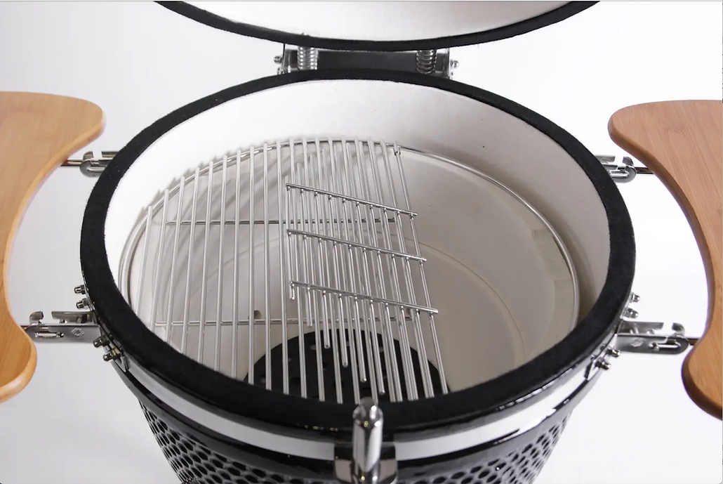 Open kamado grill showing the ceramic interior and hinged cooking grate between two wooden side shelves.