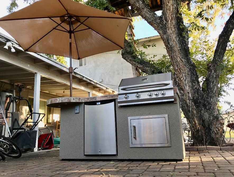 Low-angle view of Kokomo Maui Island with stainless steel grill, refrigerator, access door and round bar.