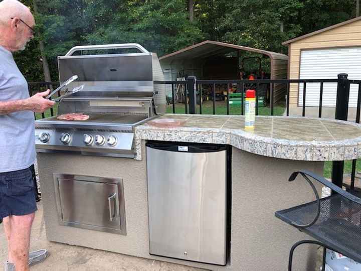 Person cooking on the open Kokomo Maui grill beside the refrigerator and curved bar countertop.