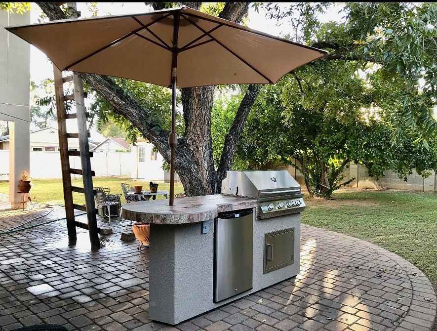 Kokomo Maui outdoor kitchen island with closed grill, refrigerator and round bar beneath a patio umbrella.