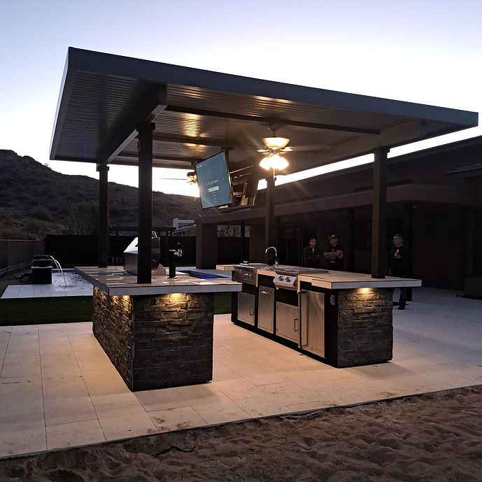 Angled view of the covered Kokomo outdoor kitchen with TV, ceiling fans, grill and stainless-steel appliances.