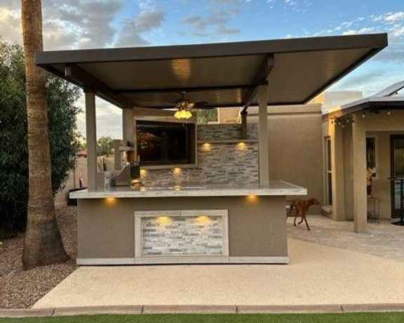 Front view of Kokomo Bermuda outdoor kitchen with roof, mounted TV and illuminated bar panels.