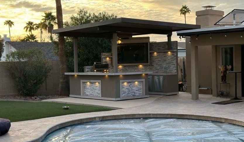  Kokomo Bermuda outdoor kitchen beside a covered pool, showing roof, TV and illuminated bar exterior.