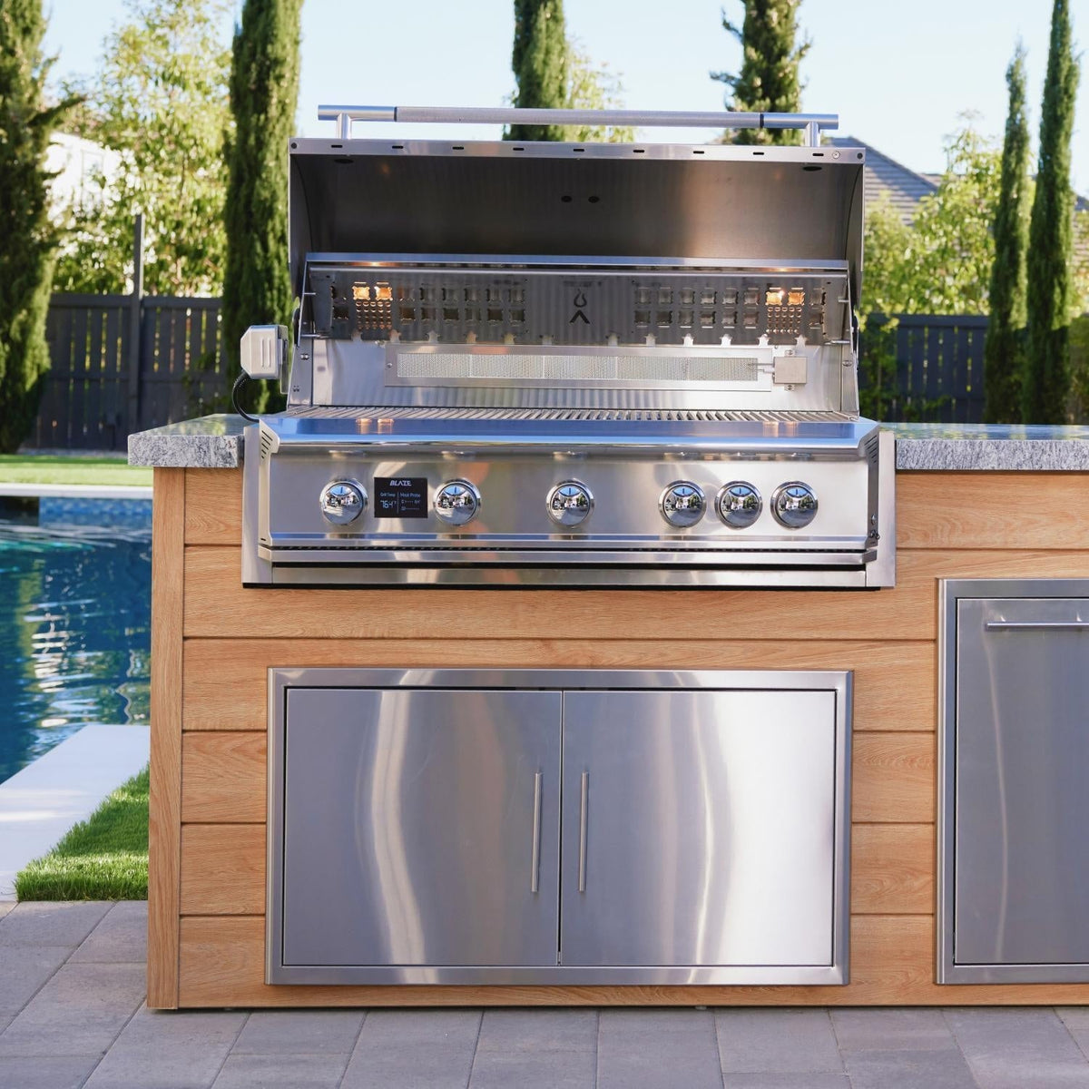 Blaze LTE PRO grill with open hood installed in a poolside outdoor kitchen island