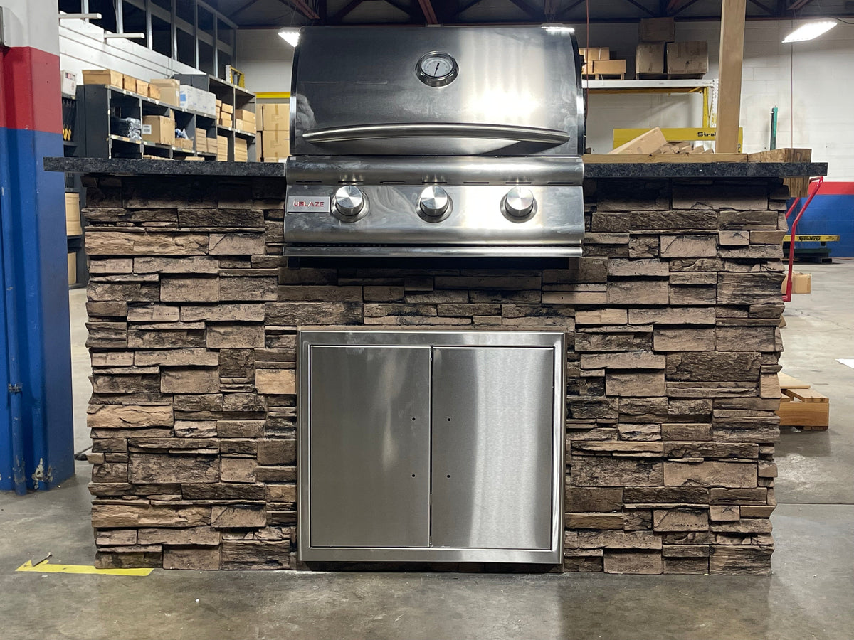 Front view of WPPO stone-faced outdoor kitchen island with Blaze three-burner grill and stainless-steel access doors.