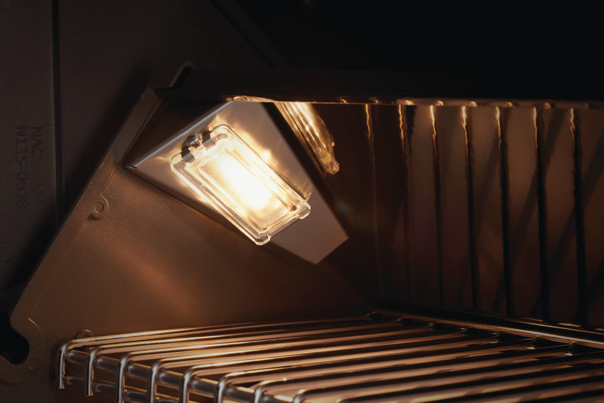 Close-up of an illuminated light inside the grill hood above the cooking grids.
