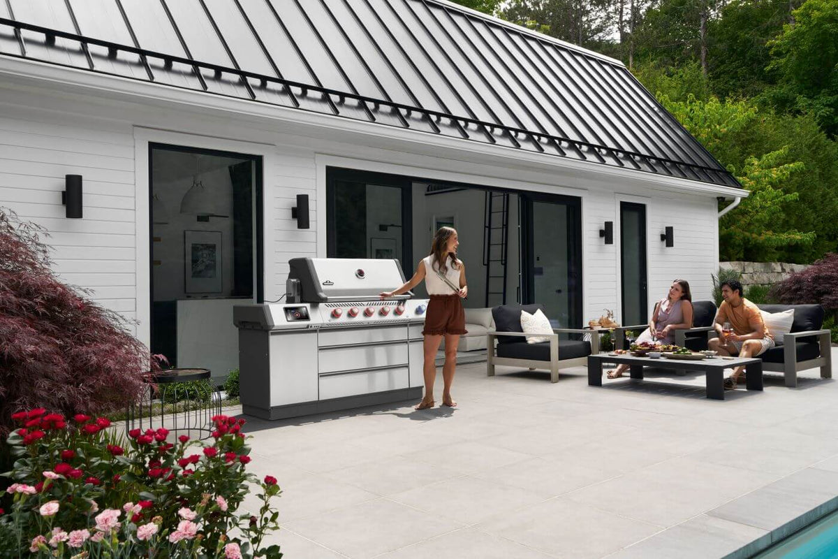 Prestige PRO 665 Elite gas grill on a patio with one person beside it and two people seated nearby.