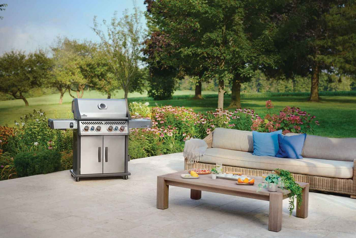Rogue PRO-S 525 RSIB gas grill with lid closed beside a sofa on a garden patio.